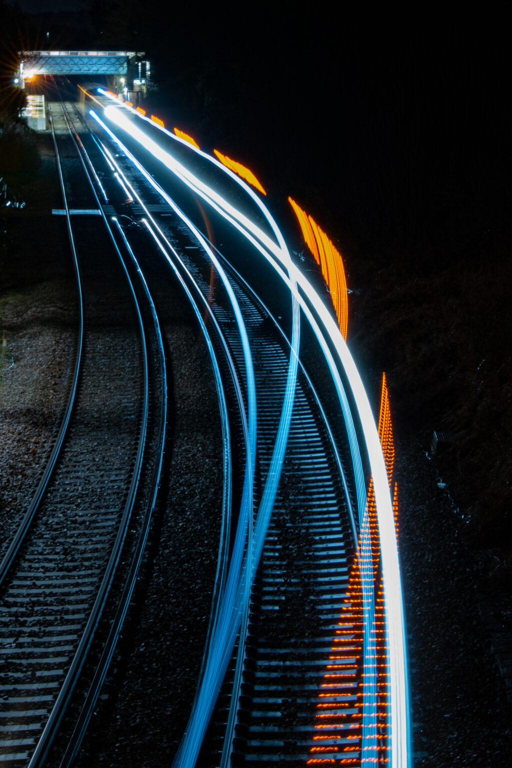 Langzeitbelichtung von Zugbewegung bei Nacht auf mehrgleisiger Bahntrasse mit Lichtspuren